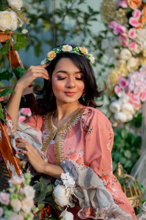 Free A woman elegantly posing with closed eyes, wearing a floral dress and flower crown, surrounded by lush blooms. Stock Photo