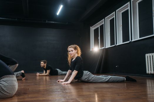 Group of young adults warming up and stretching in an indoor dance studio with wooden floor.