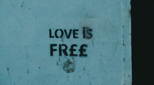 Free Graffiti artwork with 'Love is Free' message on a concrete wall, symbolizing freedom and expression. Stock Photo