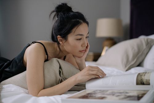Free A woman with a hair bun lies in a cozy bedroom reading a photo album, creating a serene indoor scene. Stock Photo