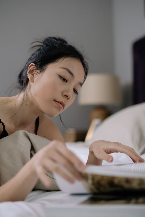 Free Young woman peacefully reading a book in bed, surrounded by a calm ambiance. Stock Photo