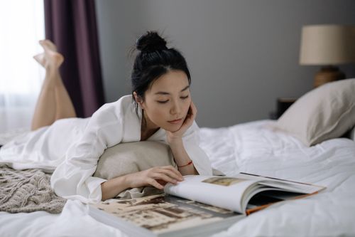Free Woman in bathrobe lying on bed, relaxing and reading a photo album at home. Stock Photo