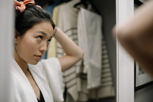 Woman in bathrobe adjusts hair in front of a bathroom mirror.