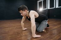 Man in Black Tank Top and Gray Pants Kneeling on Brown Wooden Floor