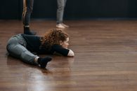 Woman in Black Long Sleeve Shirt and Gray Pants Sitting on Brown Wooden Floor