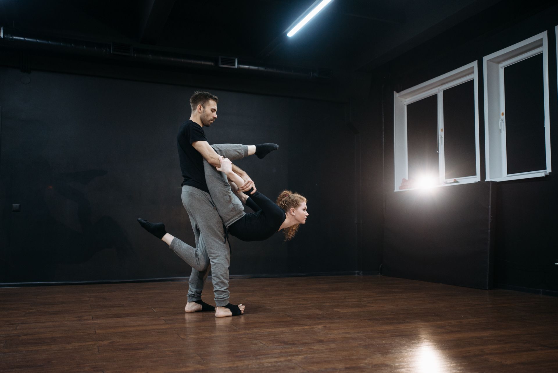 Intense dance duo in motion displaying flexibility and grace inside a dimly lit studio.
