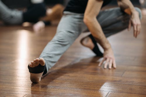 Free Person in Gray Pants and Black Shirt Stretching on the Wooden Floor  Stock Photo