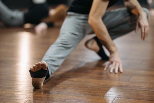 Close shot of man stretching on wooden floor, focusing on foot and hand positioning.