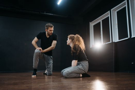 A man and a woman in casual dance wear engaged in a studio rehearsal on a wooden floor.