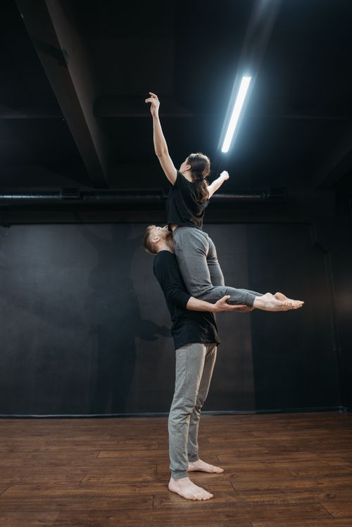 Free A couple performing a graceful yoga pose indoors with a wooden floor and dark backdrop. Stock Photo