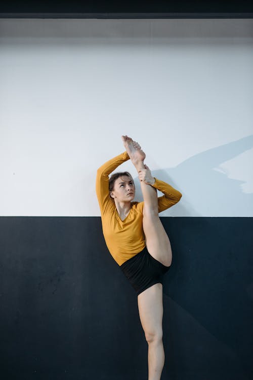 A Woman in Yellow Sweater and Black Shorts Stretching Her Legs