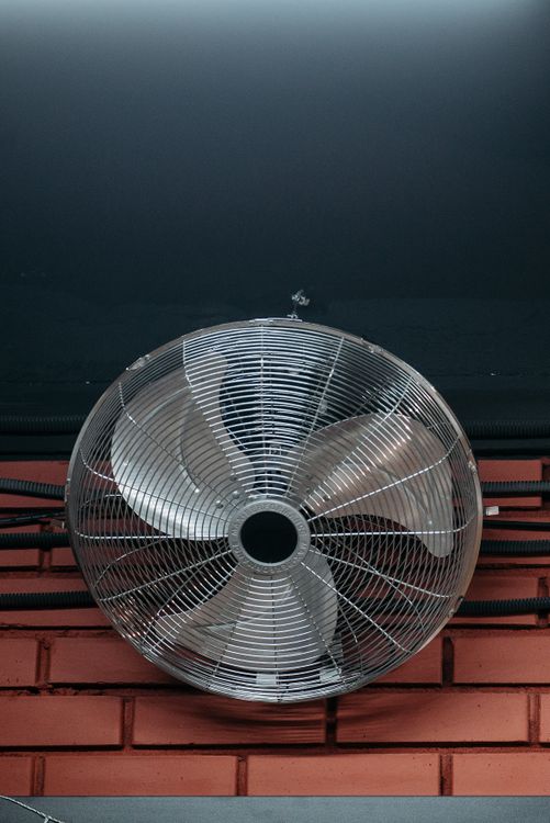 Industrial fan mounted on a brick wall, the kind used to keep air moving through a space