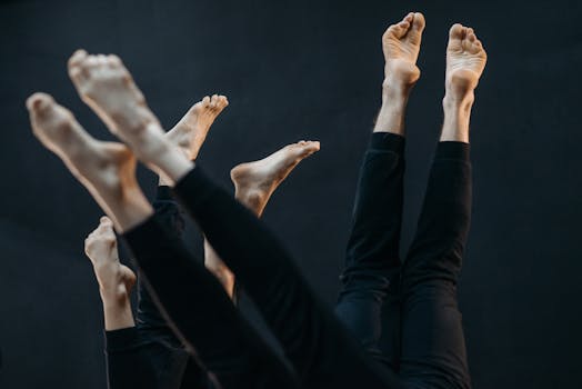 Dynamic image of multiple bare feet in black pants raised upward against a dark background.