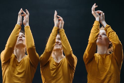 Free Three women in yellow tops reaching upward against a black background. Stock Photo