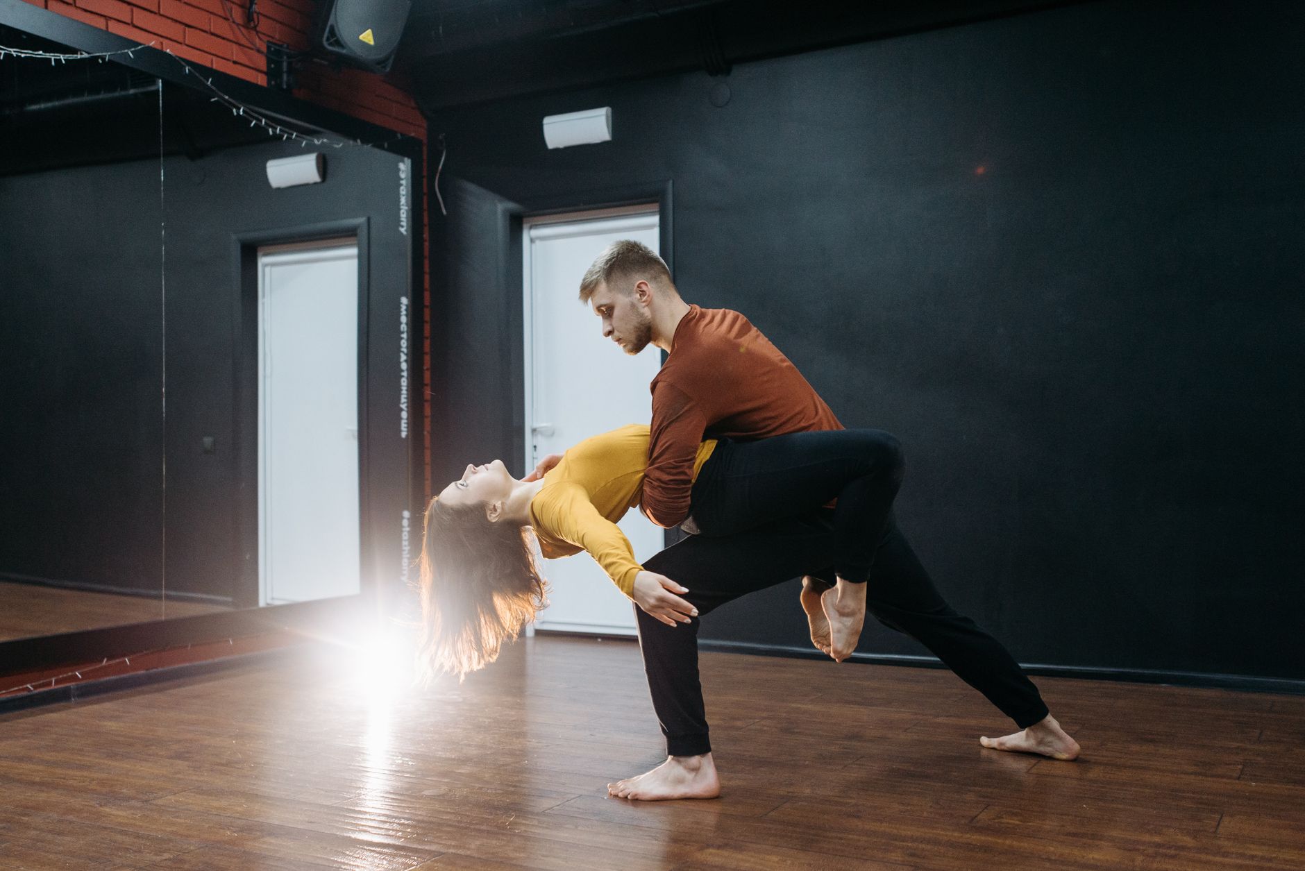 Dois adultos dançando abraçados um bolero lento em um estúdio de dança iluminado por luz amarelada