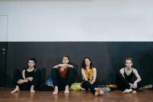 People Sitting on a Wooden Floor while Leaning on the Wall