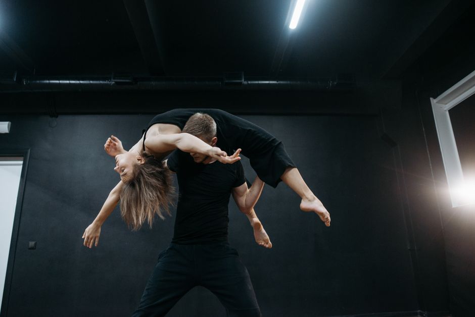 Two dancers in black outfits perform an impressive lift in a studio setting.