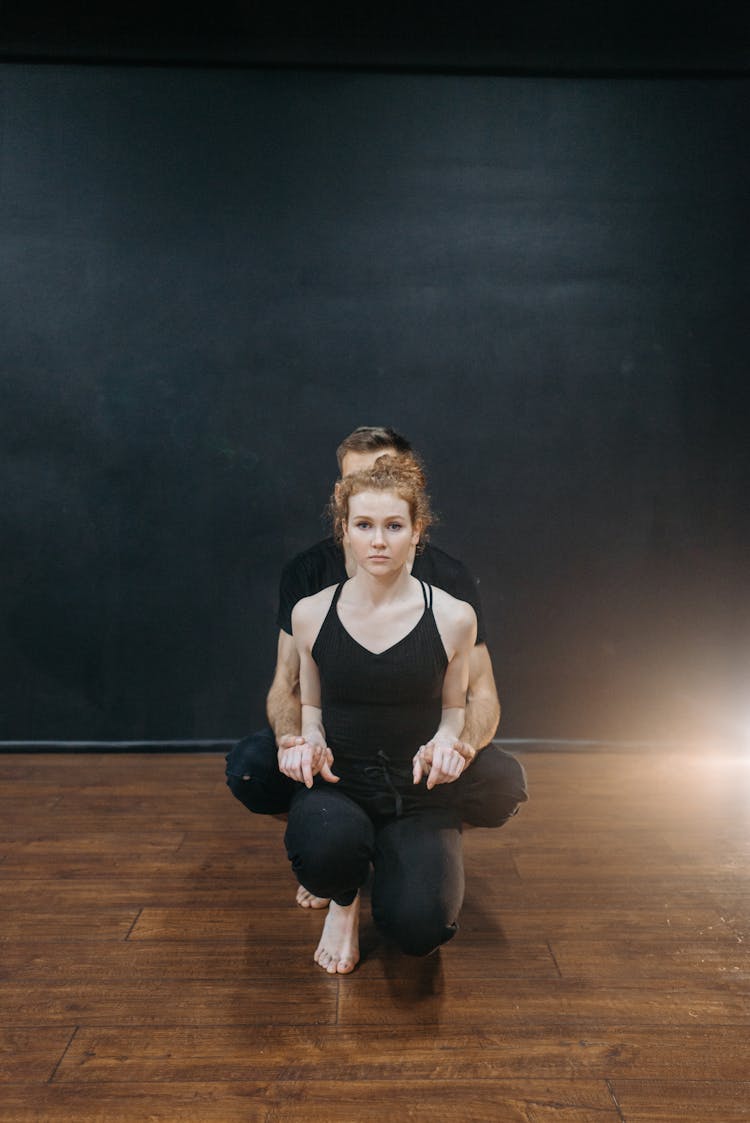 A Woman In Black Tank Top And Black Pants Sitting On Wooden Floor