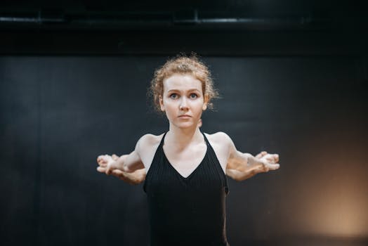 Woman stretching indoors with a focused expression, arms extended, in a black tank top.