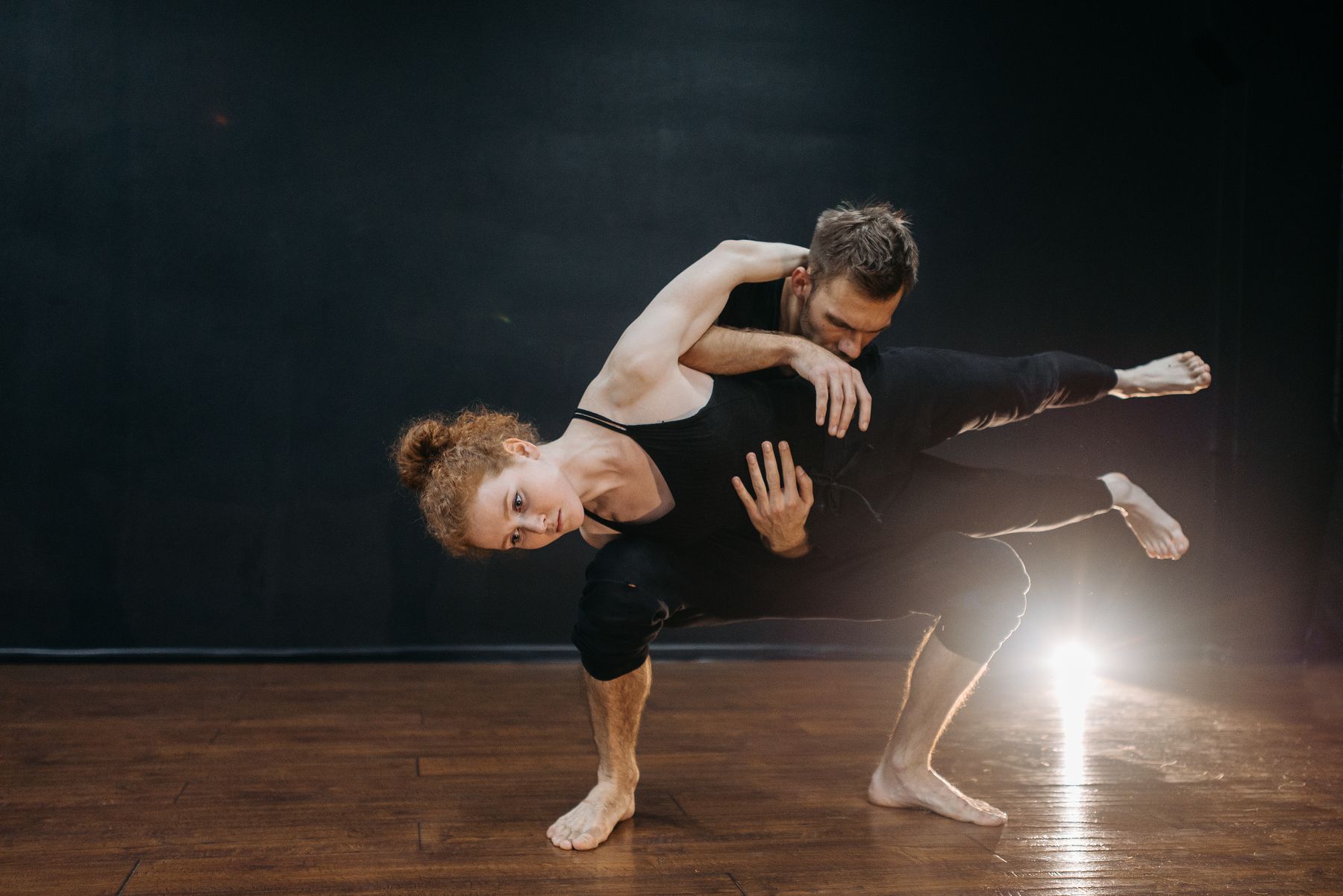 Pareja de danza contemporánea en un movimiento de suelo, con un foco al fondo