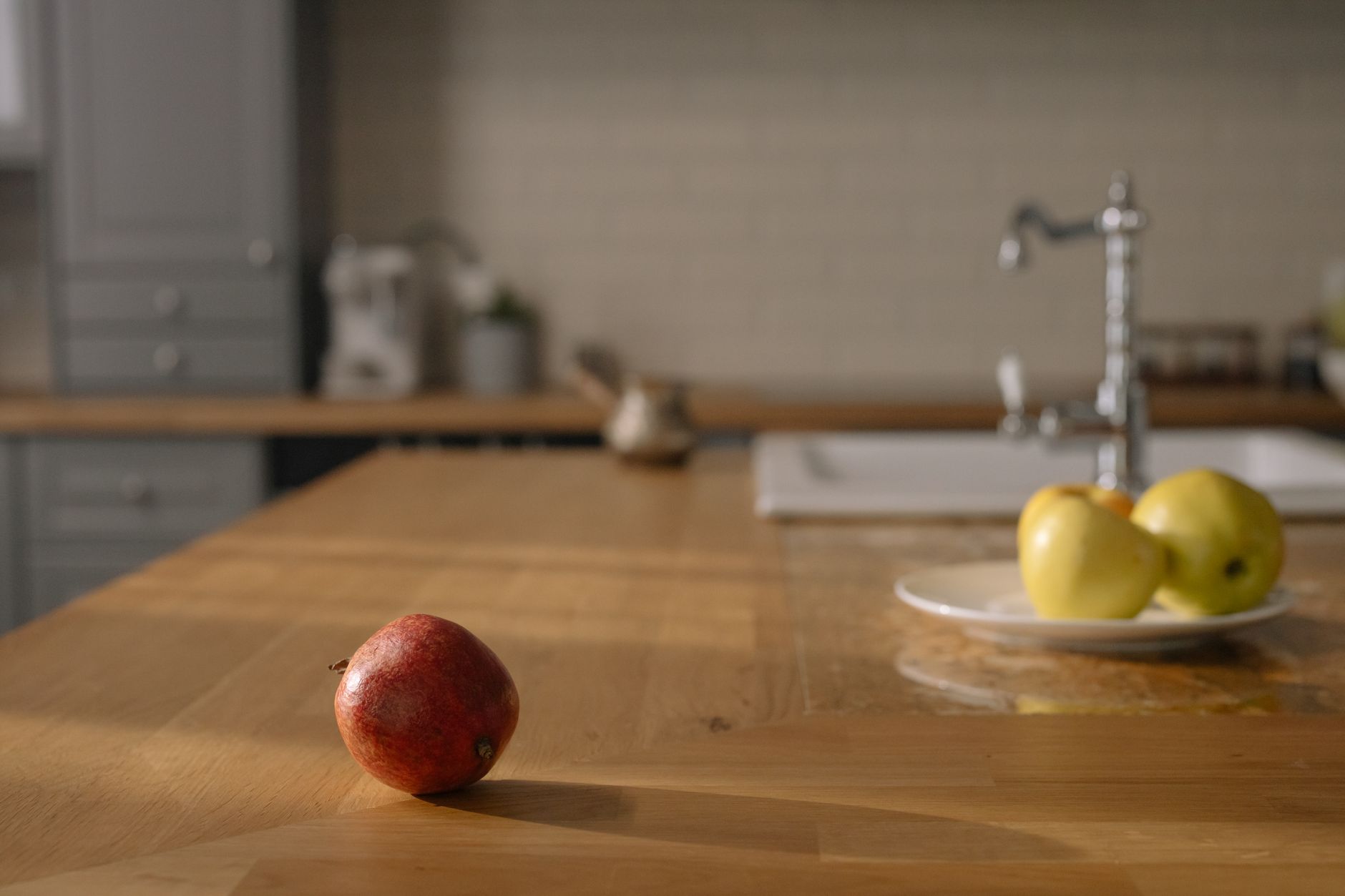 CLEAN TEC SERVICES - A red apple on a wooden counter and yellow apples on a plate in a cozy kitchen.