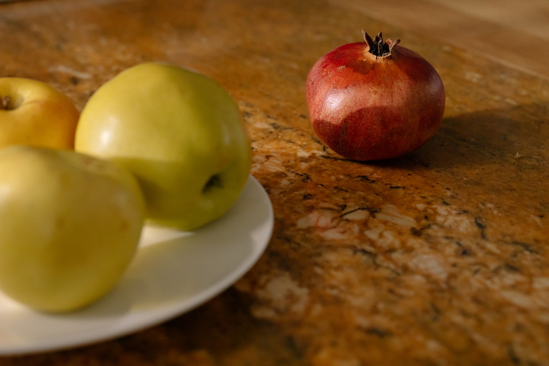 Artistic still life with apples and pomegranate on granite surface creating a warm, natural feel.