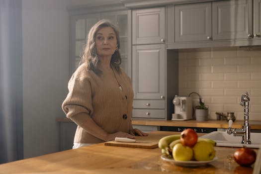 Elegant elderly woman in a cozy kitchen setting with natural lighting and a bowl of fresh fruit.