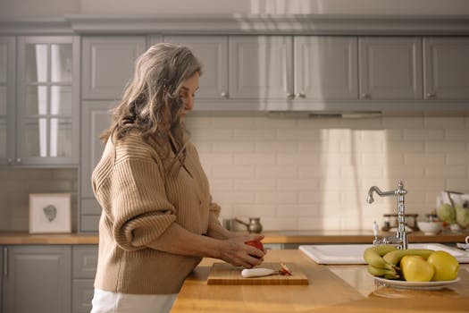 Senior woman slicing fruit in a warm kitchen setting, showcasing home cooking.