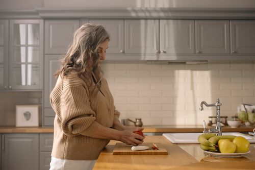 Free Senior woman slicing fruit in a warm kitchen setting, showcasing home cooking. Stock Photo