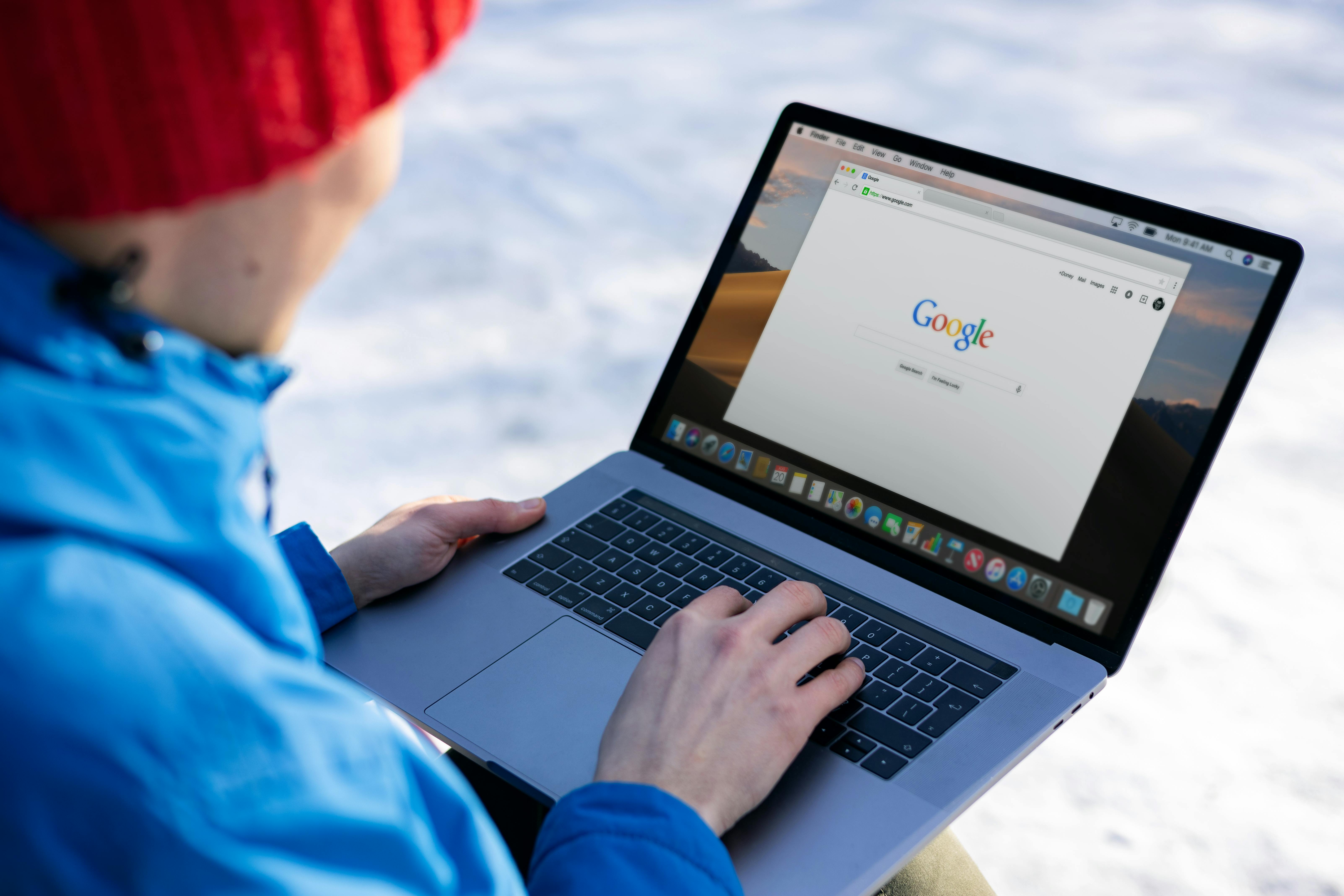 Person in winter gear using a laptop with a Google search on screen outdoors.