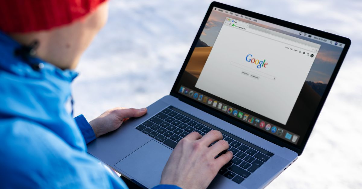 Pessoa com roupas de inverno usando um laptop com uma pesquisa no Google na tela ao ar livre.
