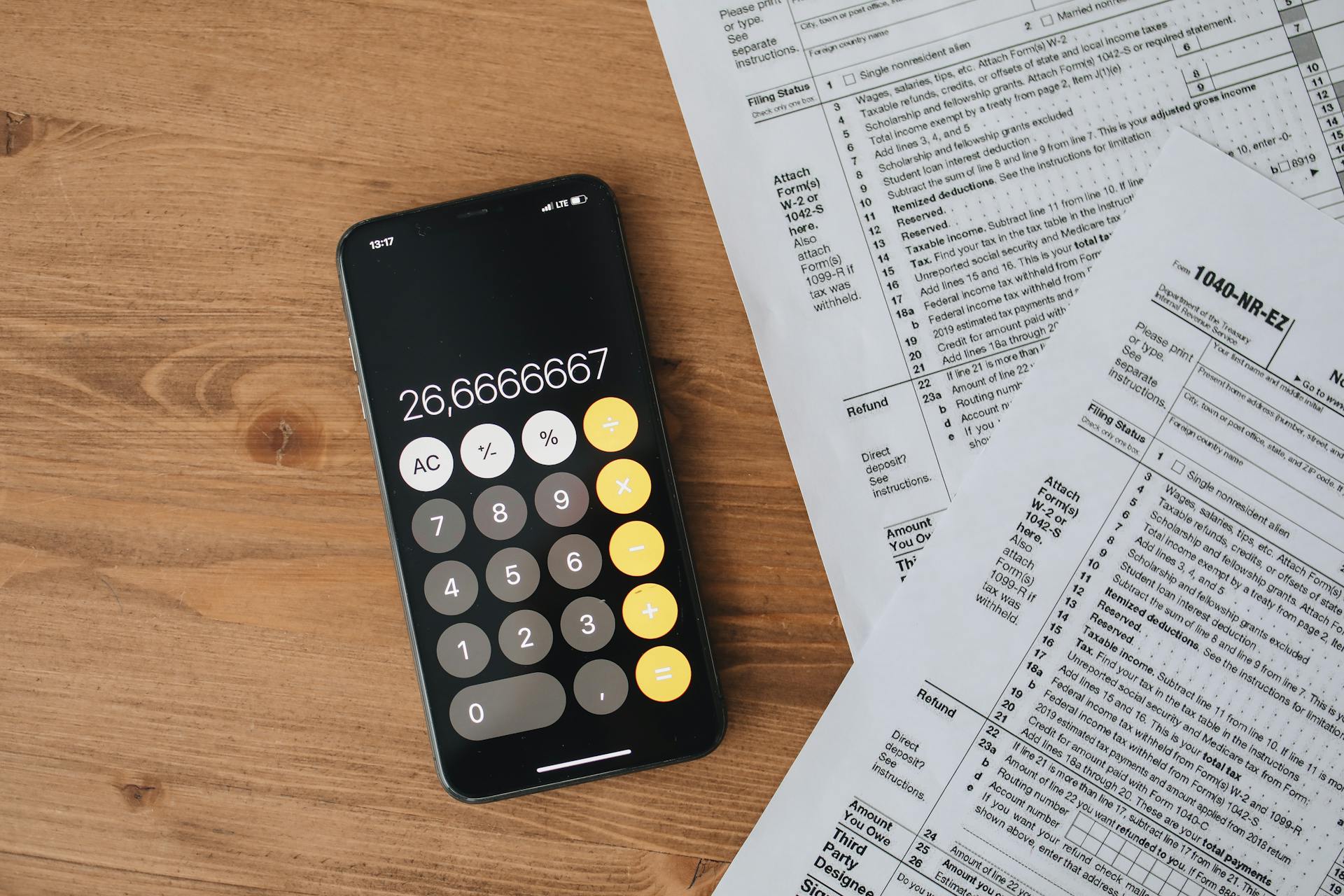 Overhead view of smartphone calculator and tax forms on a wooden table.