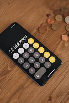 Top view of a smartphone calculator app with coins on a wooden surface, representing finance and calculations.