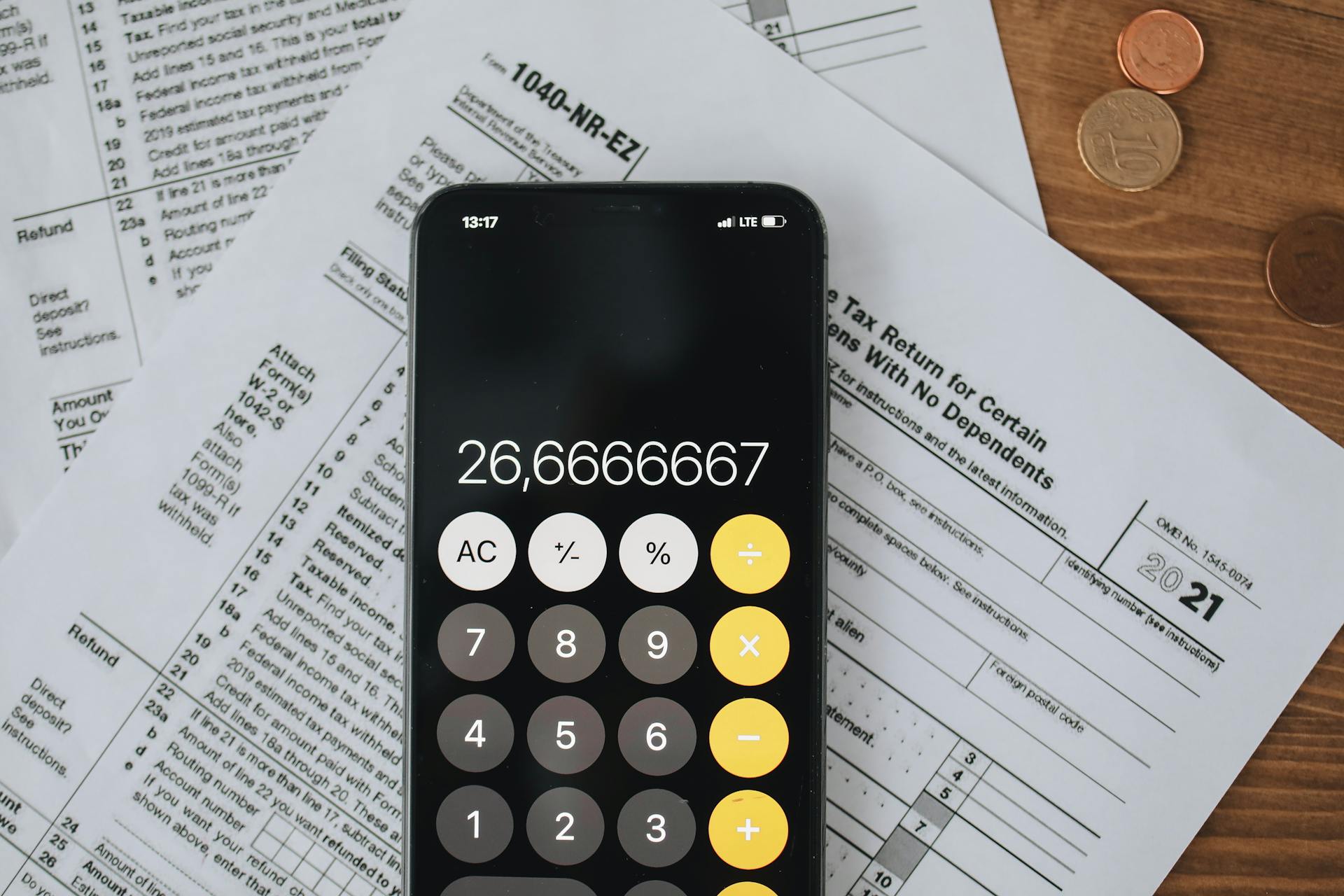 Smartphone calculator over tax forms with coins, symbolizing tax calculation and finance.