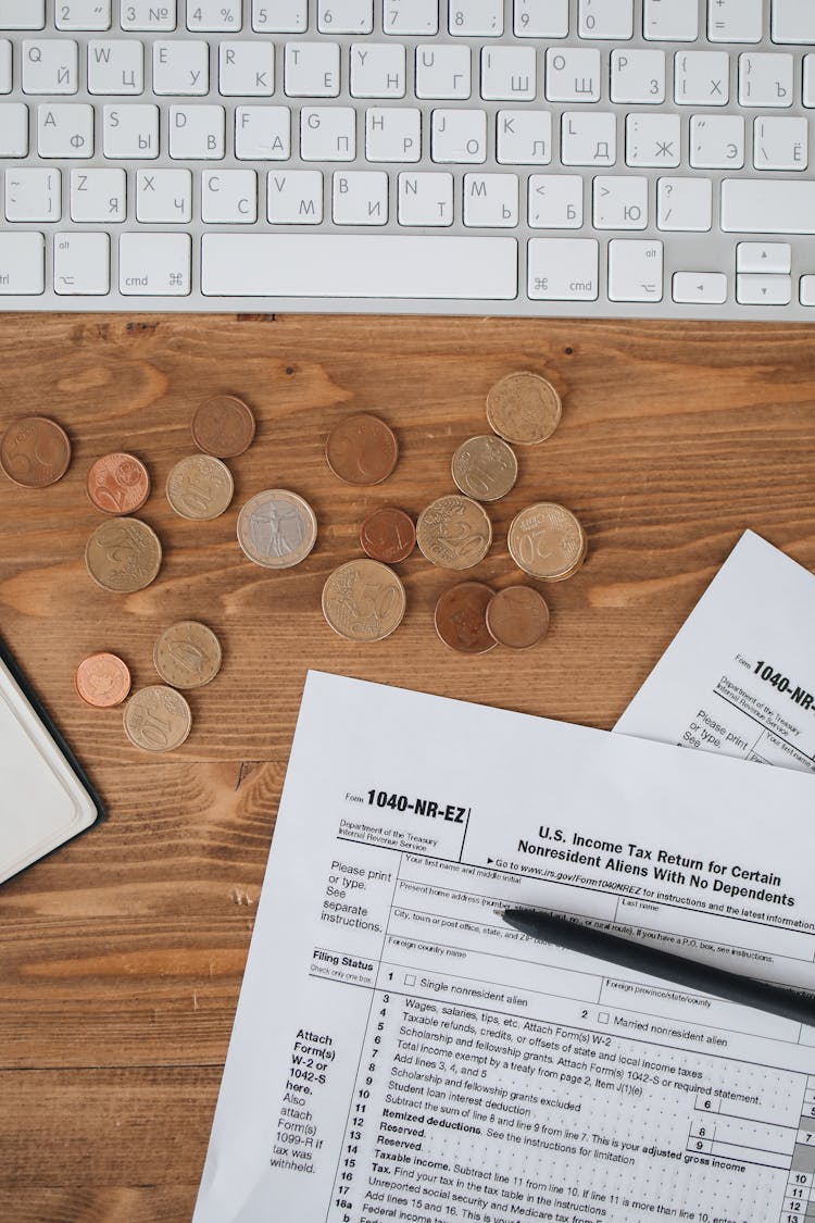 Income Tax Forms With Pen And Coins ON Wooden Surface