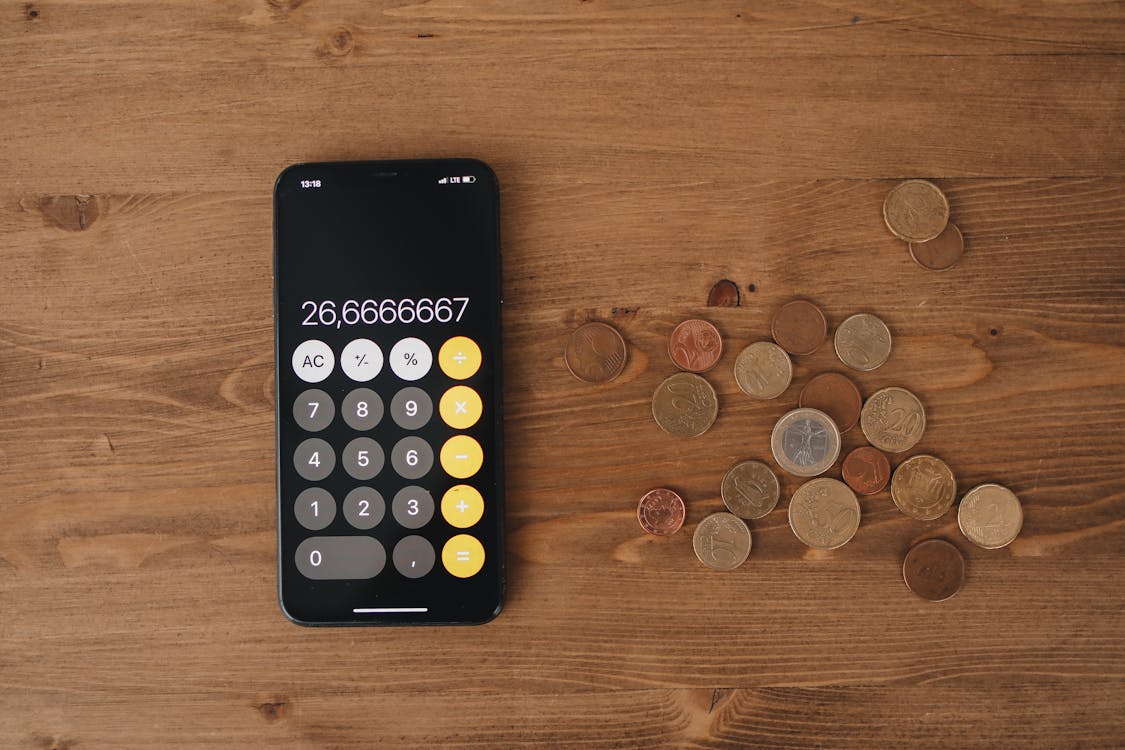Black Calculator And Loose Change On Wooden Surface