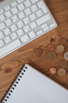 Organized workspace showing a keyboard, coins, and notebook on a wooden table.