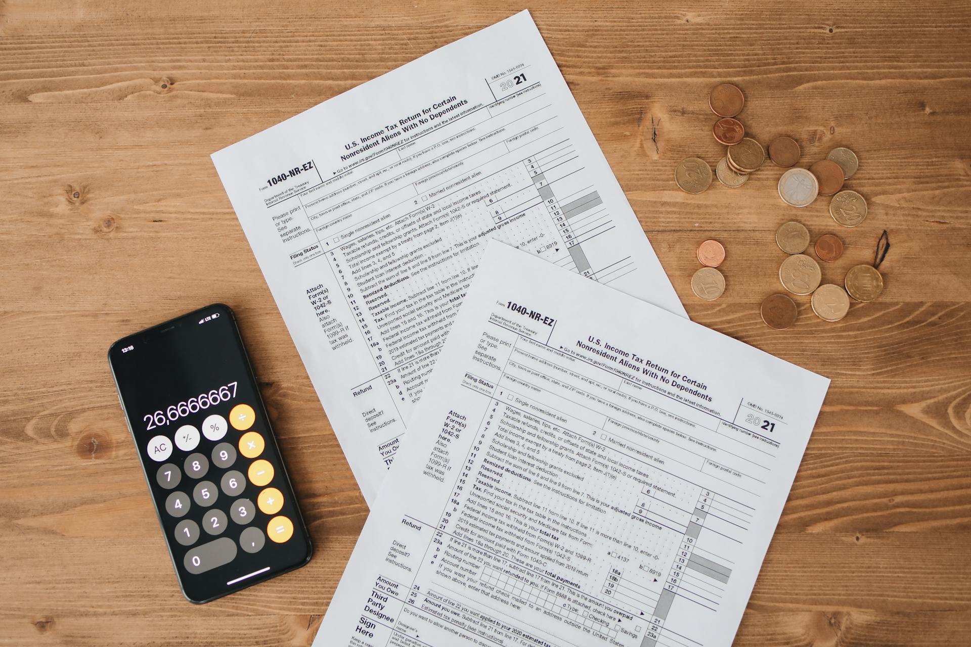 Top view of tax documents, calculator, and coins on wooden table.