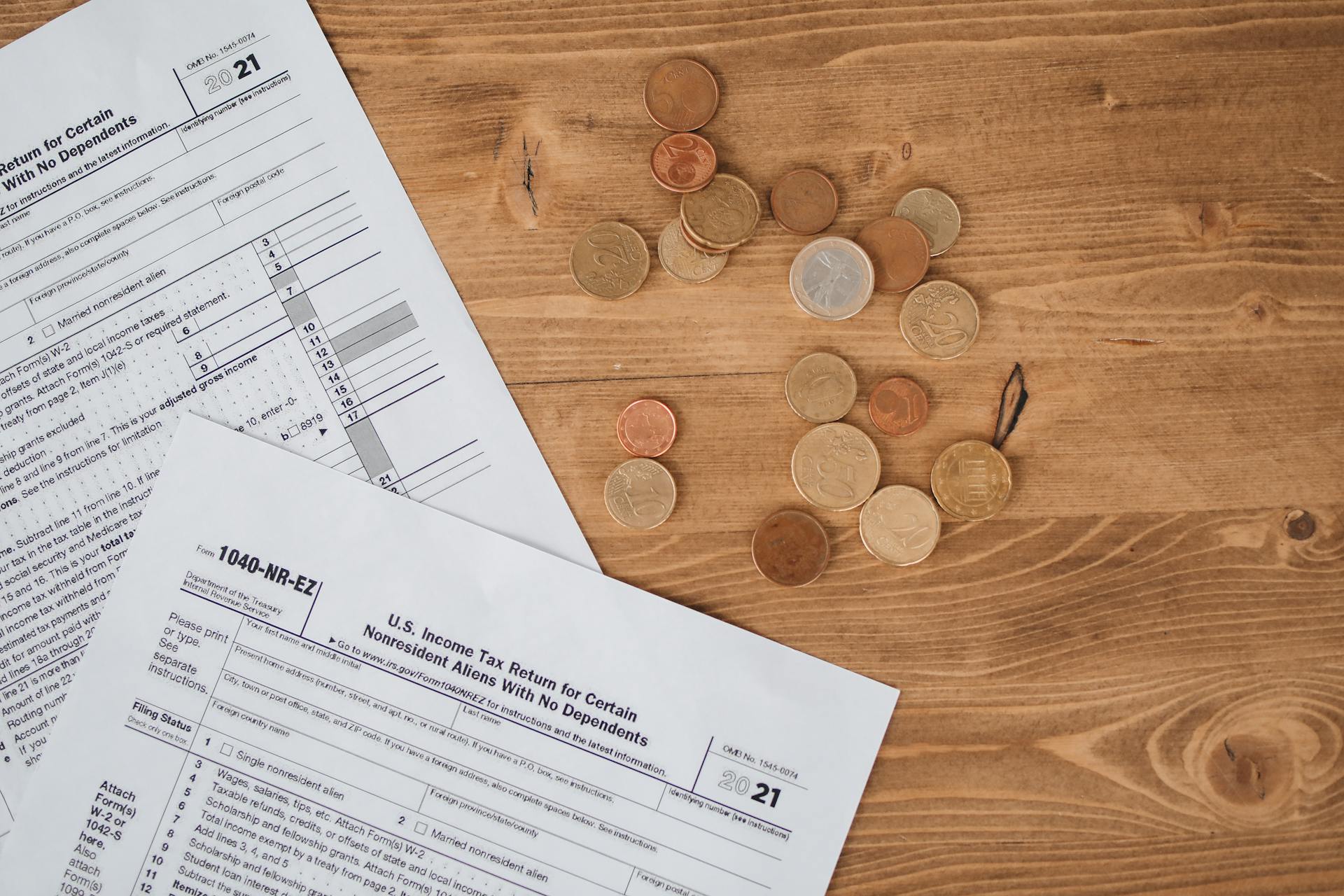 Flat lay of tax forms and scattered coins on a wooden table, illustrating finance and taxation concepts.