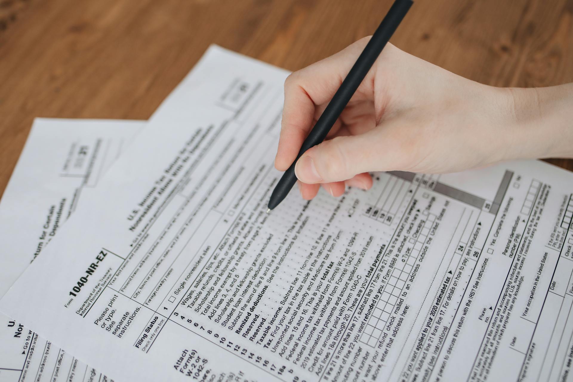 Close-up of a hand writing on tax documents with a black pen.