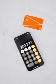 Top view of a smartphone displaying a calculator app next to an orange credit card on a white surface.
