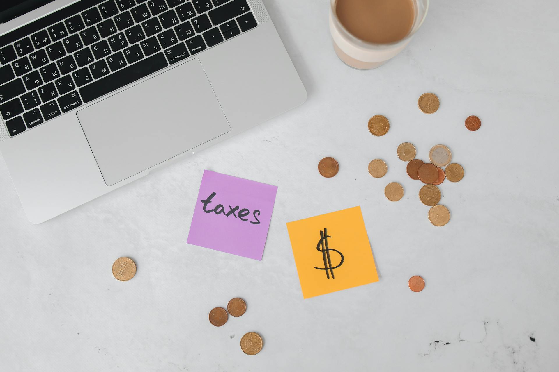 A workspace with a laptop, sticky notes, coins, and a coffee cup, ideal for tax planning.