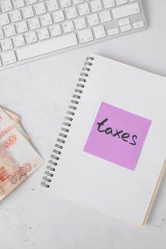Notebook labeled with taxes, cash, and a keyboard on white surface, ideal for financial concepts.