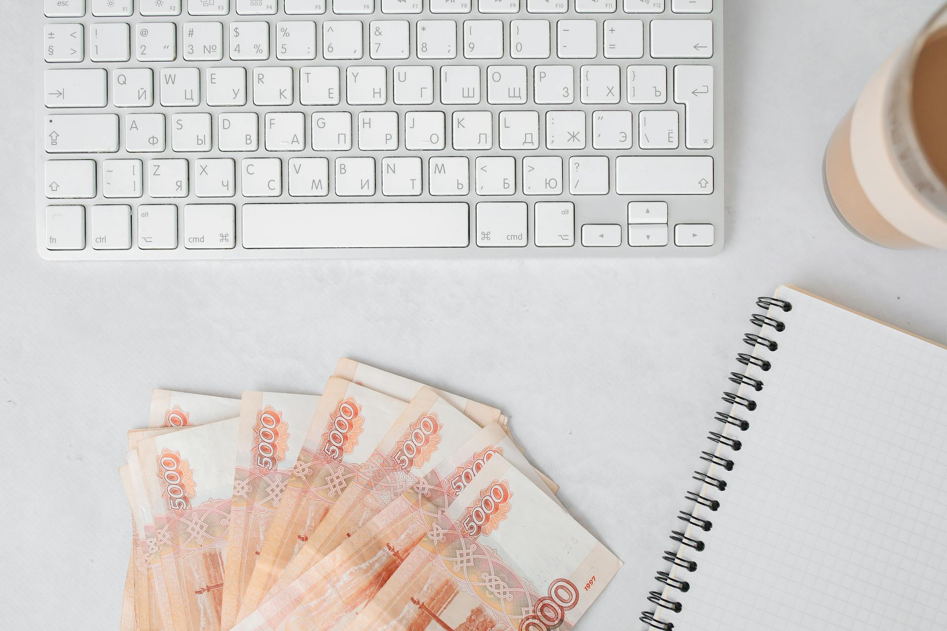 Russian banknotes with a keyboard and notebook on a white table surface, ideal for business finance themes.