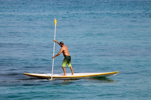 A Shirtless Man Standing while Paddling on a SUP Board