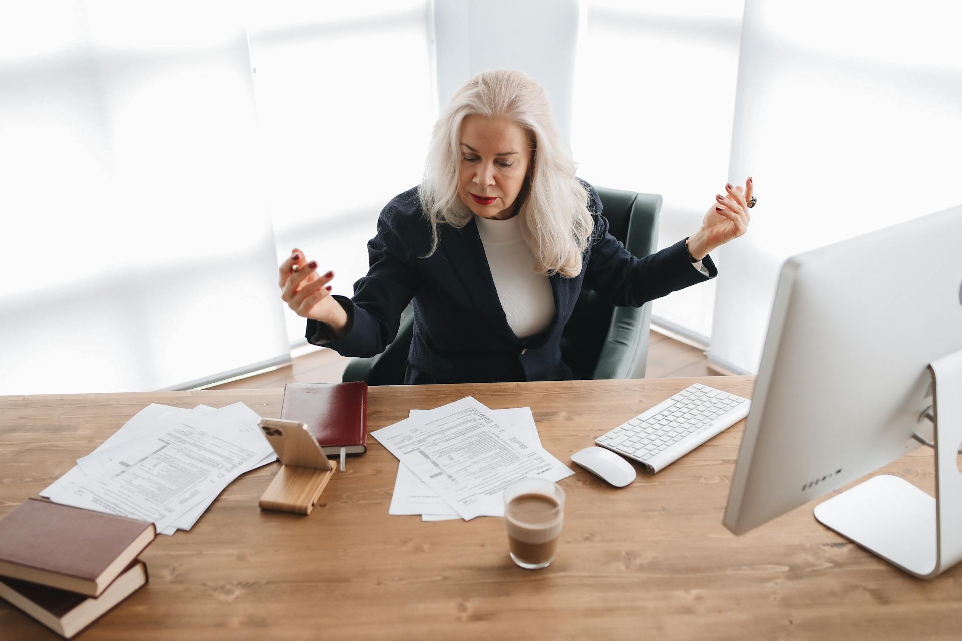 Focused senior woman with gray hair working on financial documents at her office desk with a computer.