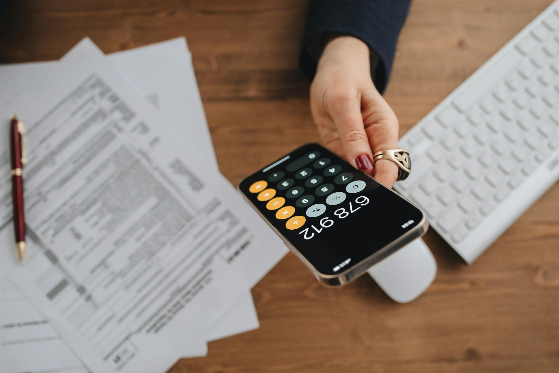 Hand holding smartphone calculator over tax documents on desk.