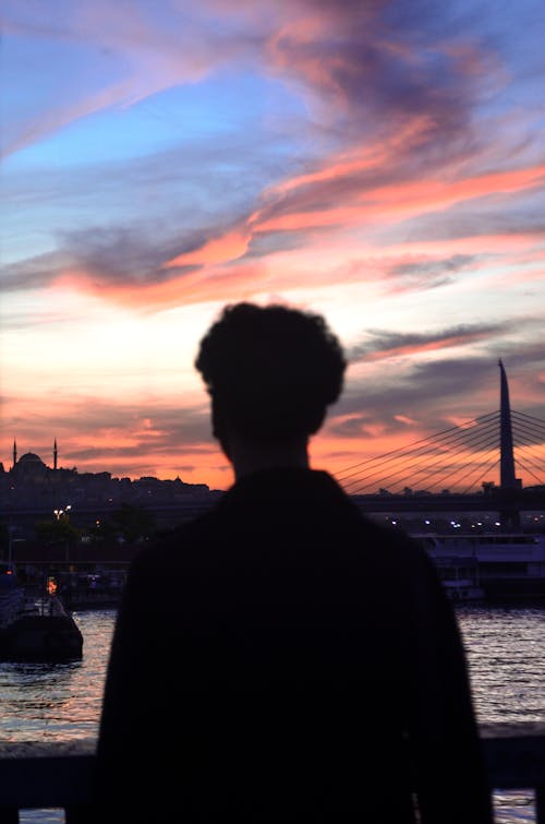 Free Back view of unrecognizable male traveler standing on river embankment and admiring picturesque sunset over Istanbul Stock Photo
