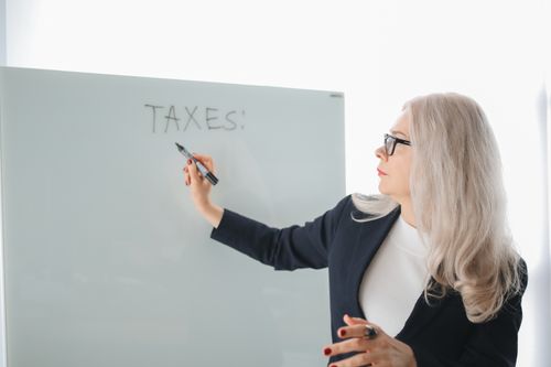 Free Senior woman writing on whiteboard during a tax discussion in office setting. Stock Photo