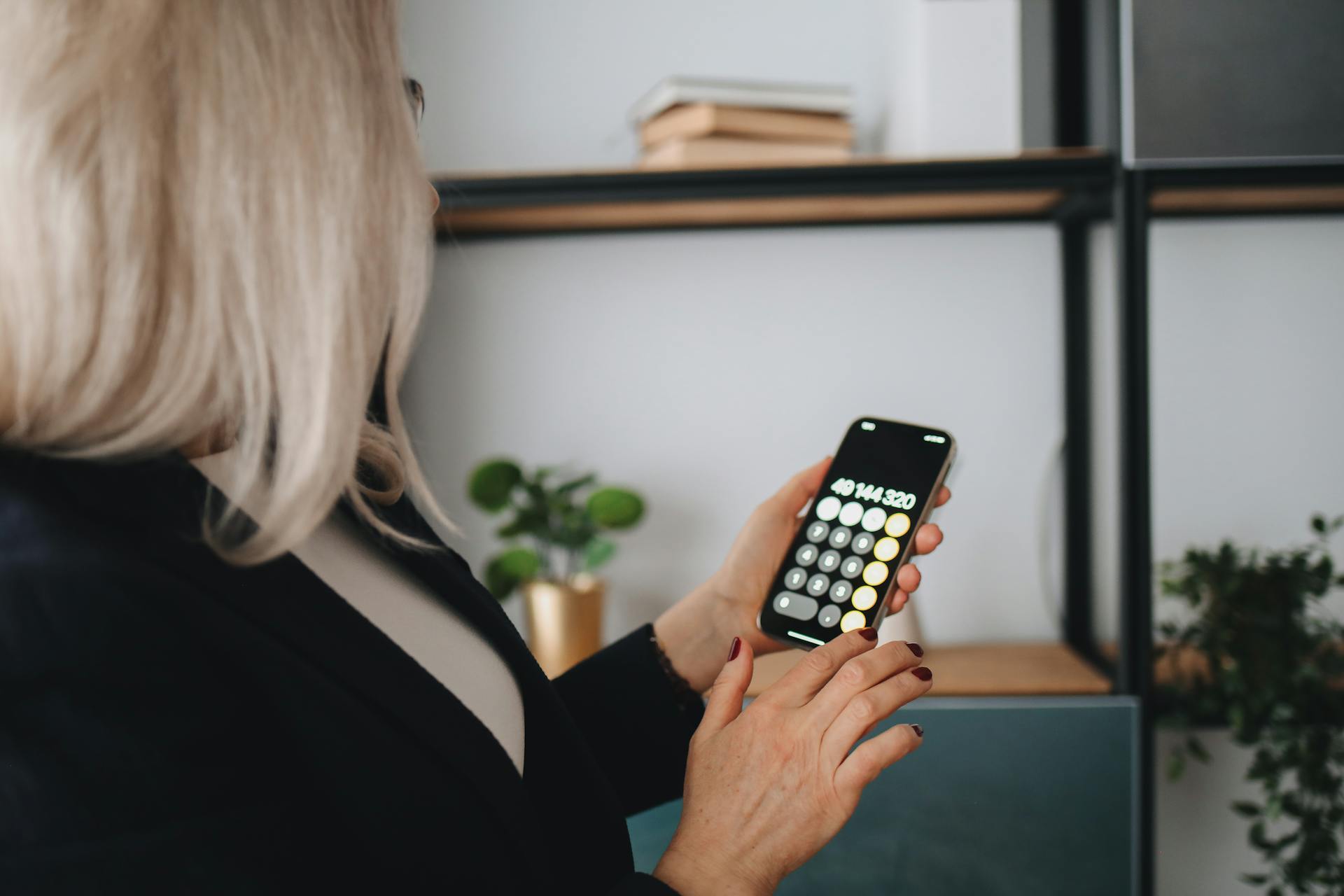 A businesswoman using a smartphone calculator indoors, focusing on screen display.